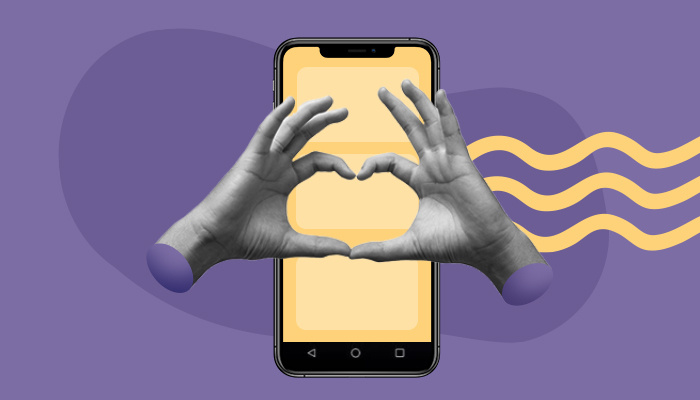 A imagem mostra duas mãos sobrepostas a um smartphone. Juntas, elas formam o gesto que representa um coração.